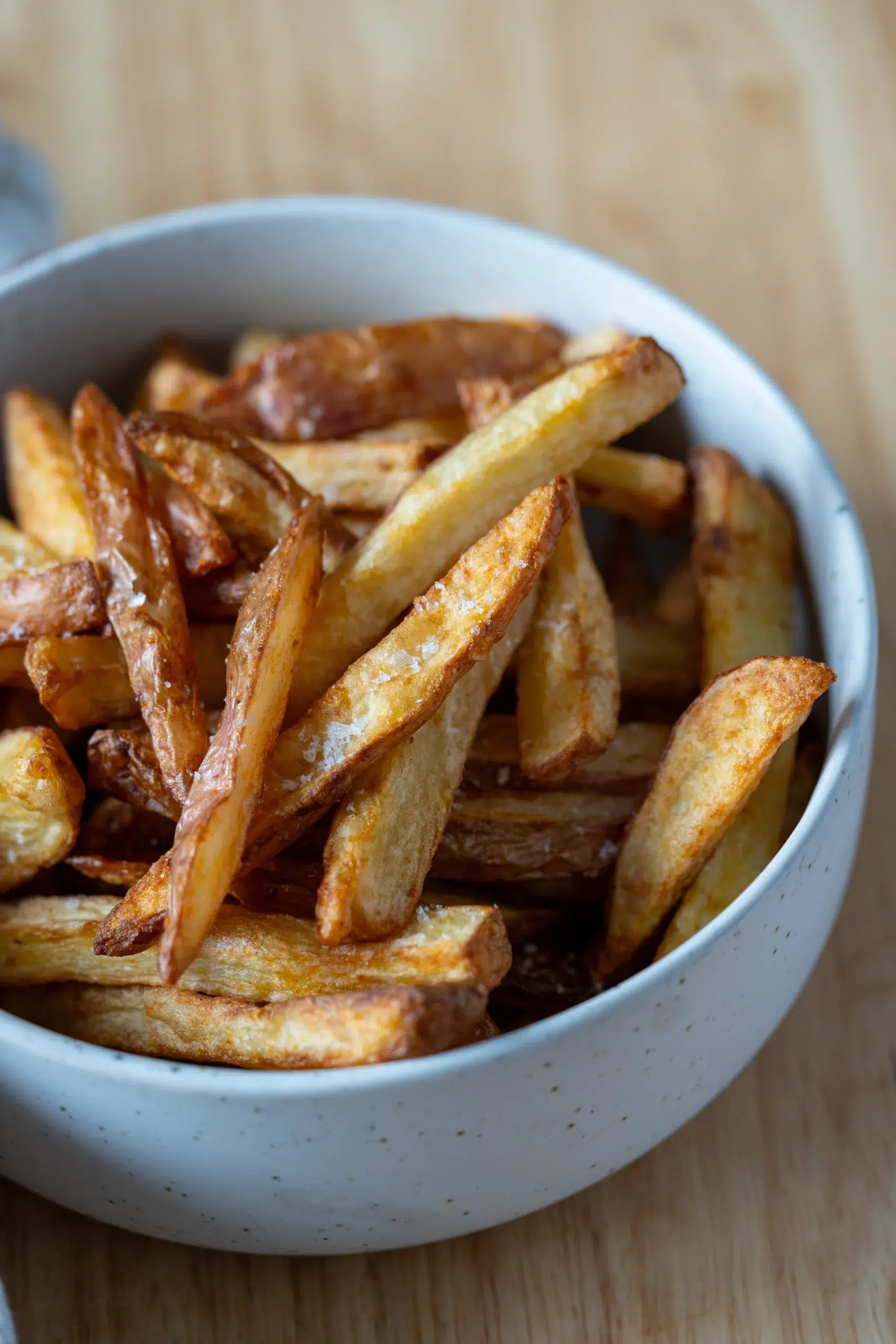 Side view of golden, crispy air fryer chips in a white bowl, showing crunchy texture