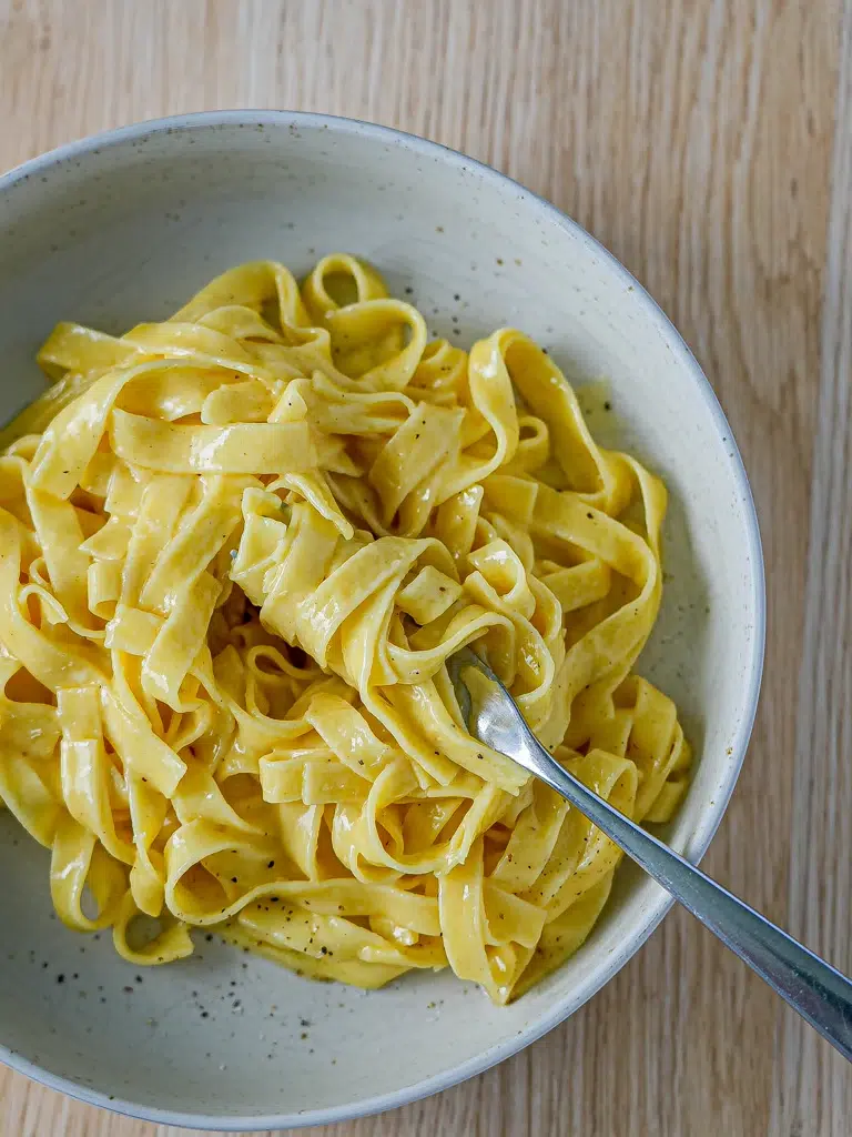 A plate of authentic fettuccine Alfredo with a twisted forkful, topped with freshly cracked black pepper.