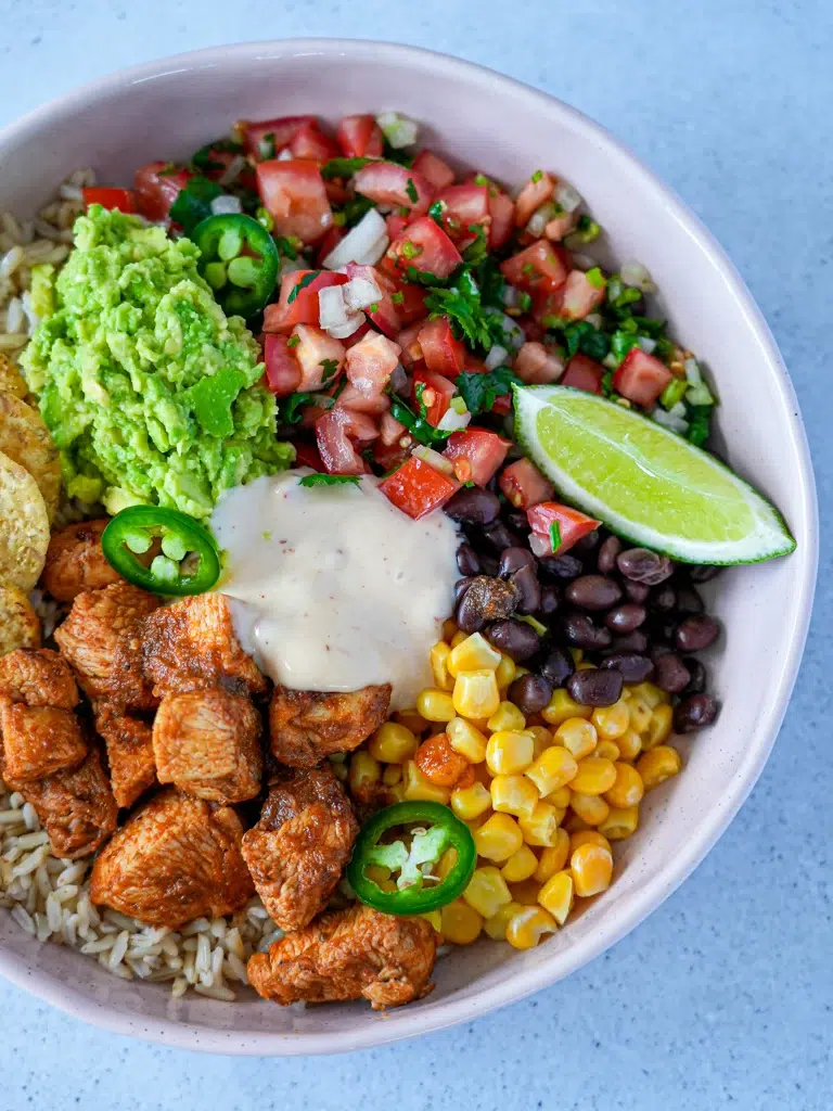 Close-up of Colorful chicken burrito bowl filled with seasoned chicken, rice, black beans, corn, diced tomatoes, and avocado, garnished with cilantro