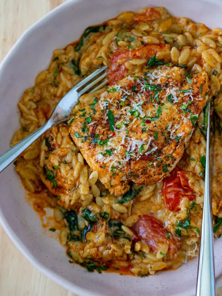 Chicken with creamy red pesto risoni in a serving bowl with spoon and fork