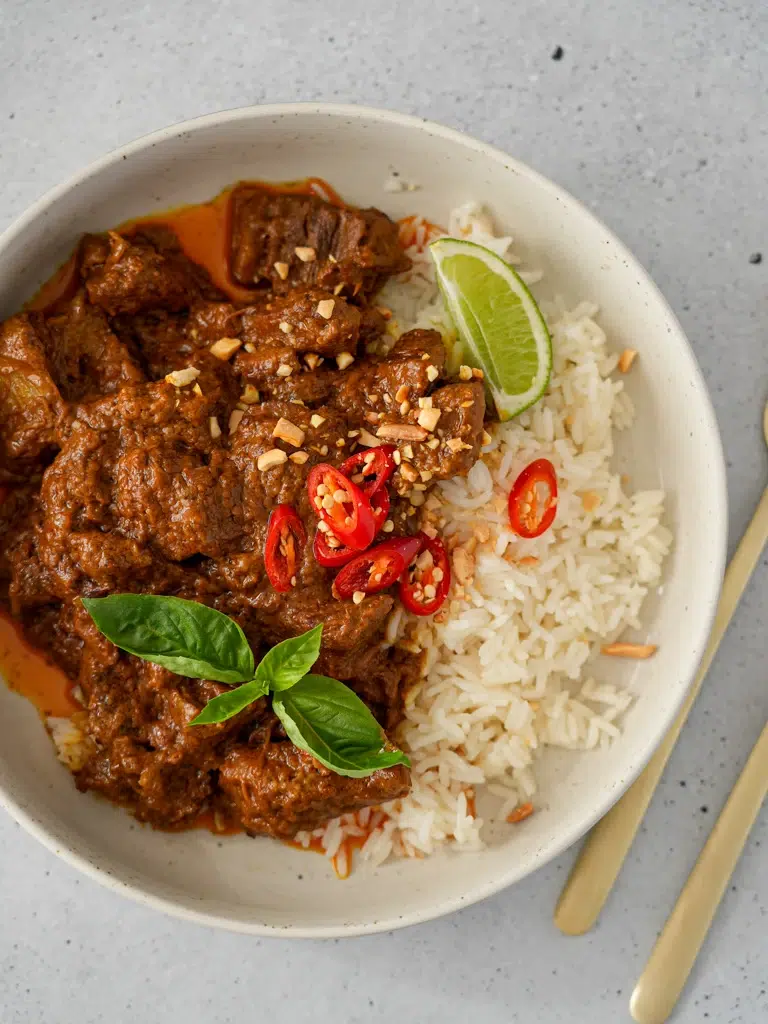 Coconut Beef Curry served in a bowl with fresh herbs and a side of rice
