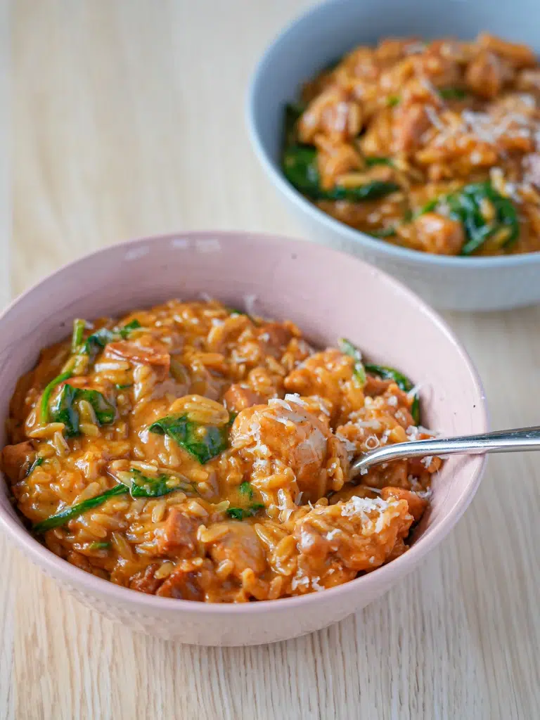Bowl of creamy chicken and chorizo risoni (orzo) with a spoon in action, capturing the creamy texture and colorful ingredients