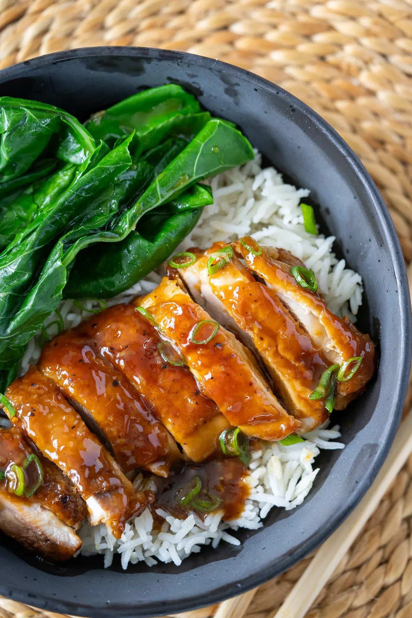 Bowl of honey garlic chicken and rice with fresh greens, paired with chopsticks for serving.
