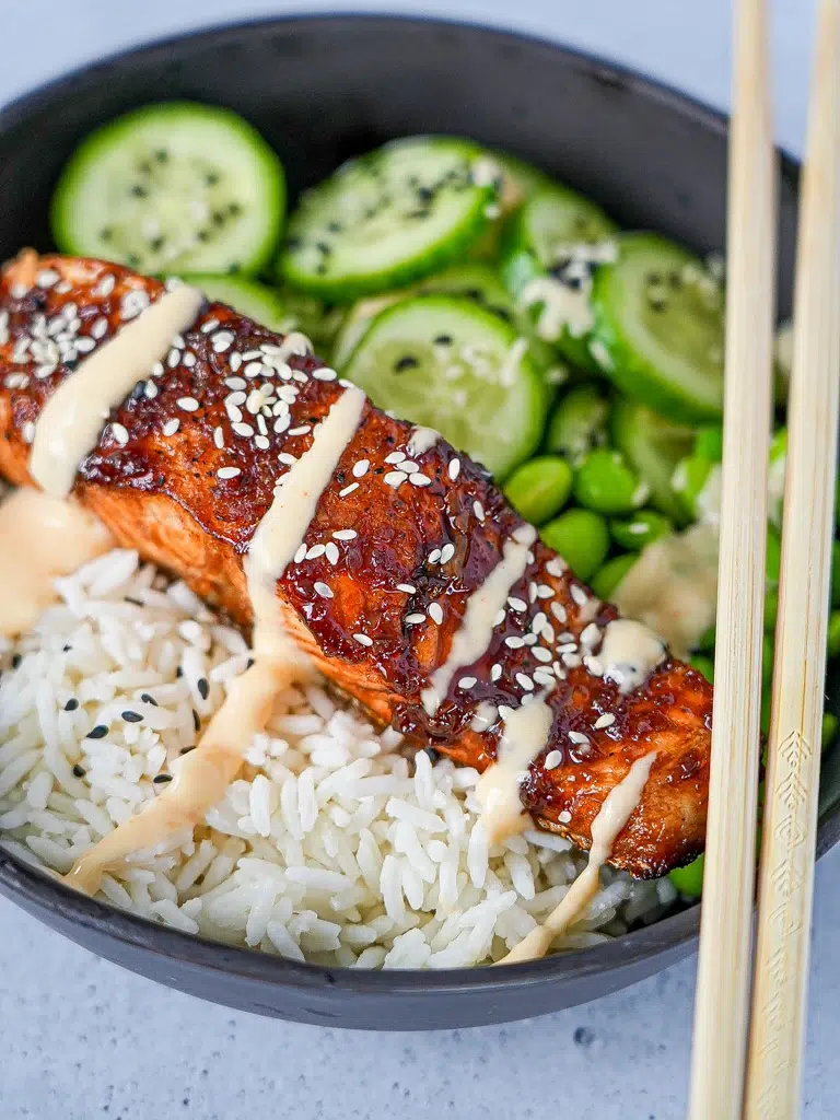 Bowl of honey soy glazed salmon fillet topped with sesame seeds and green onions, served with a side of steamed rice and vegetables