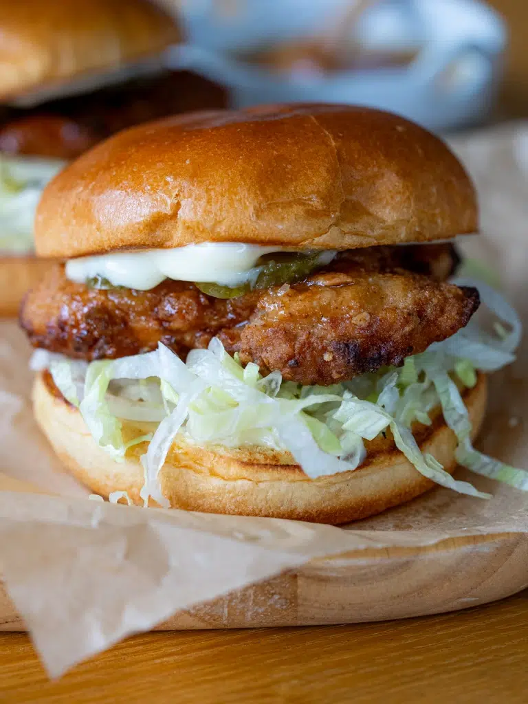 Close-up of a hot honey crunch chicken burger with crispy fried chicken, shredded lettuce, pickles, and mayonnaise in a soft brioche bun.