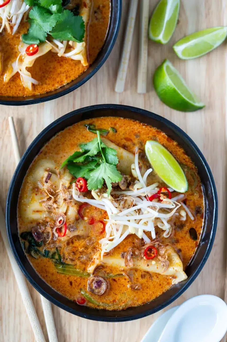 Dumpling laksa soup in a black bowl with lime and chopsticks on the side